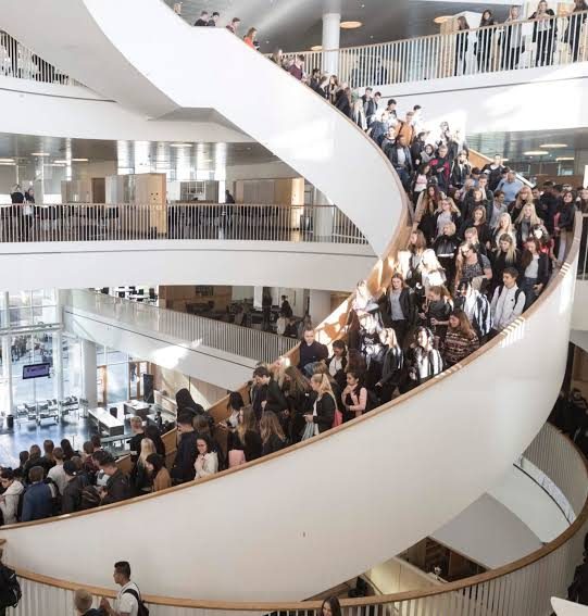 מדרגות ספירלה דרמטיות שמתפתלות כלפי מעלה במרכז בניין פתוח עם מרפסות לכל קומה, עיצוב מודרני.
